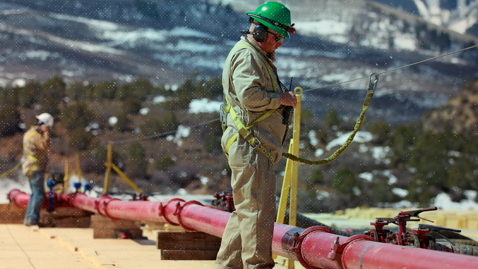 A worker stands over a pipe at the site of a natural gas hydraulic fracturing and extraction operation.