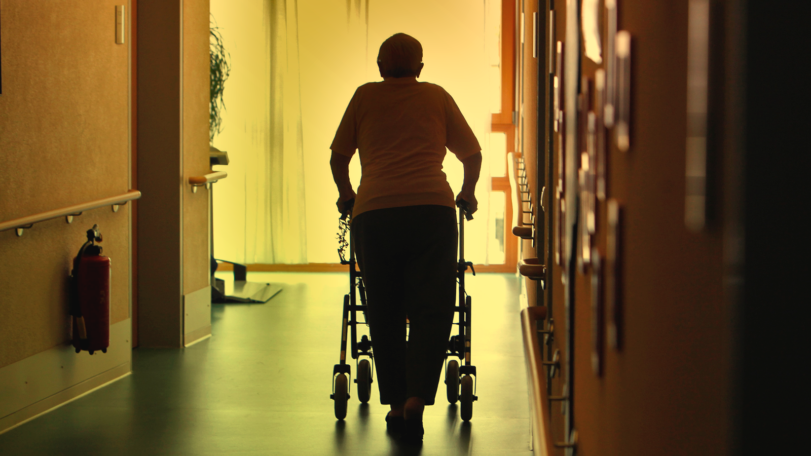 An elderly person uses a walker in the hallway of a nursing home.