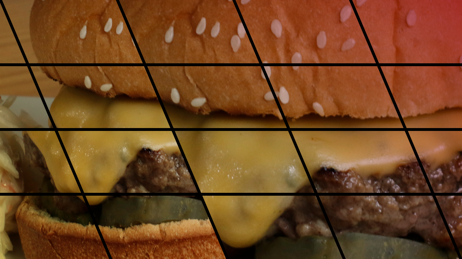 An up-close of a cheeseburger, showing a sesame seed bun, melted cheese, a beef patty, and pickles.
