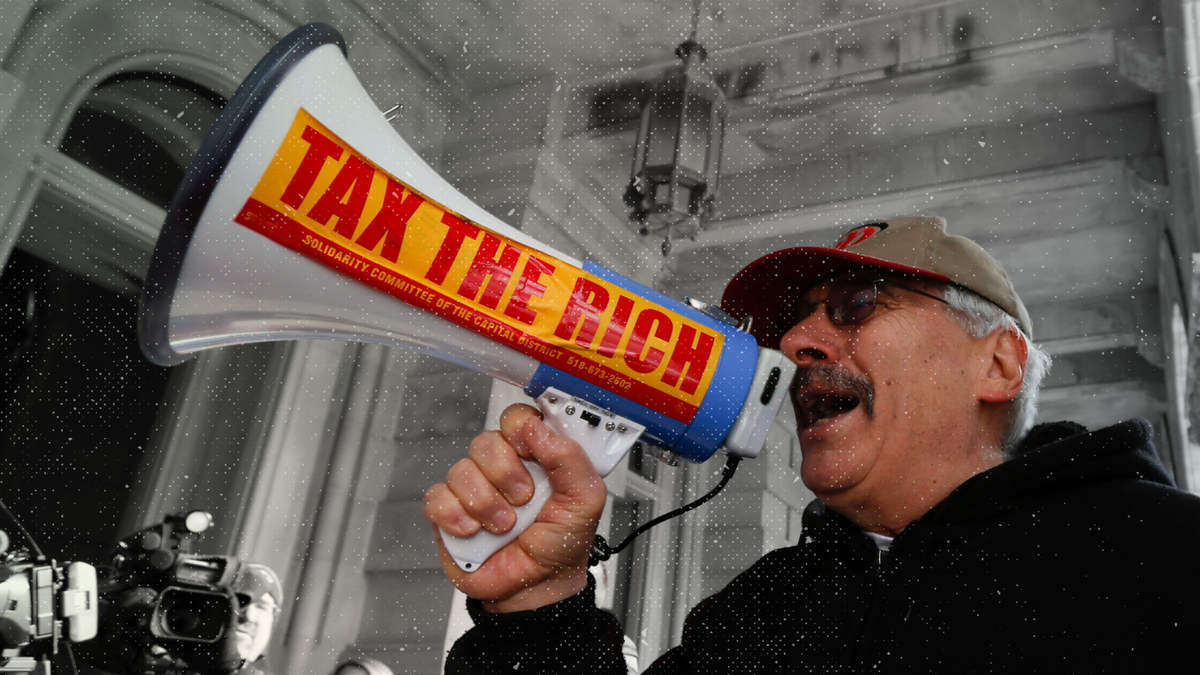 A man yells into a loudspeaker with a "Tax The Rich" sticker on it at a protest.